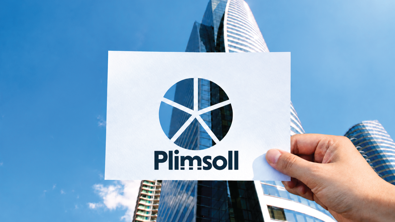 Hand holding a Plimsoll card with a cut-out pie chart divided into five segments, revealing parts of the same office building behind each segment.